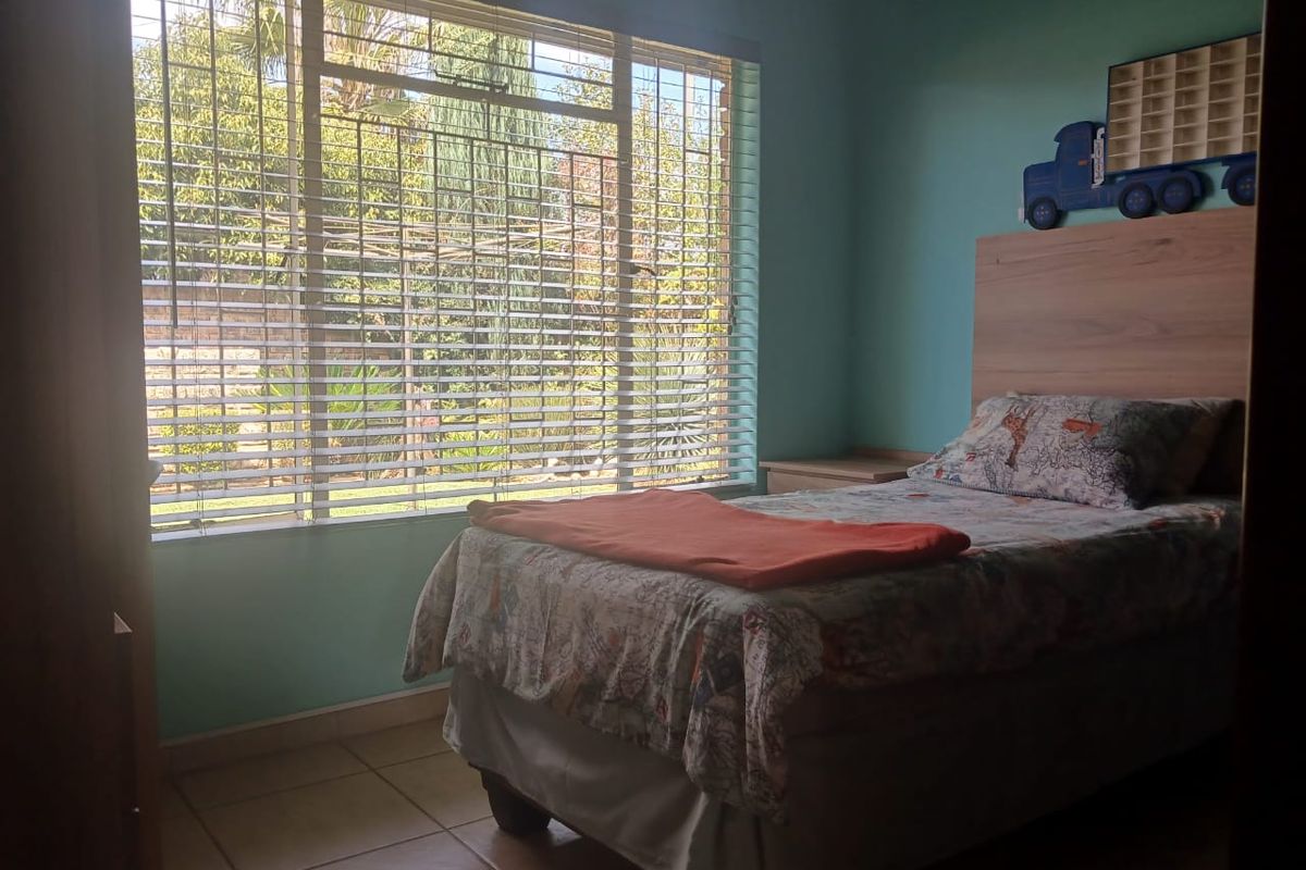 A bedroom featuring tiled flooring, a built-in headboard, and large windows with venetian blinds allowing natural light.