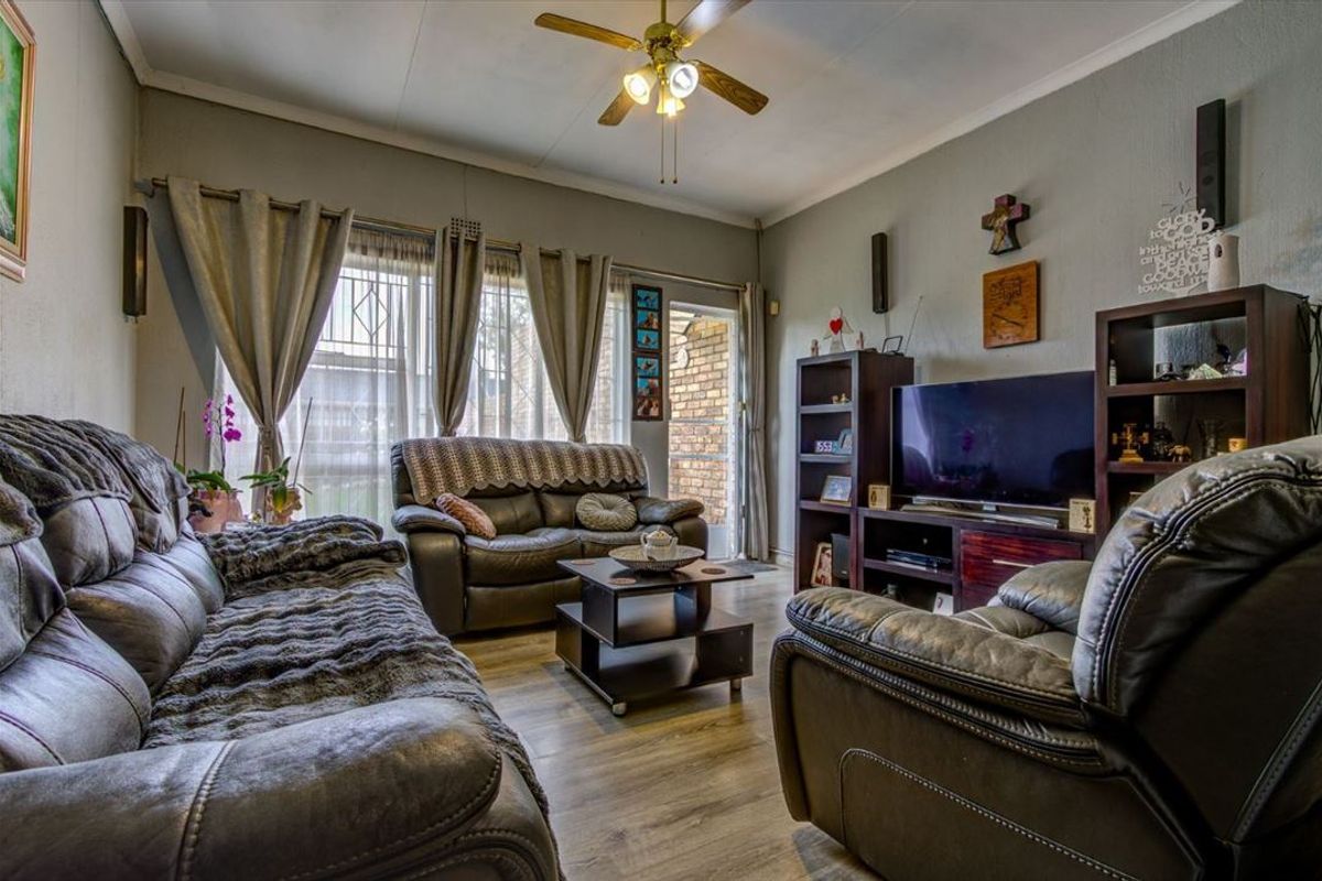 A comfortable living room featuring laminate flooring, a ceiling fan, and direct access to the exterior through a sliding door with security gate.