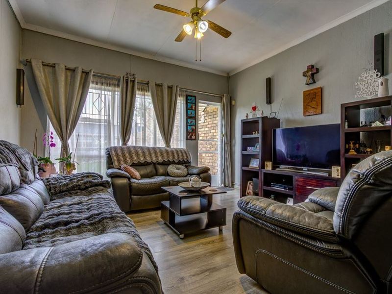 A comfortable living room featuring laminate flooring, a ceiling fan, and direct access to the exterior through a sliding door with security gate.