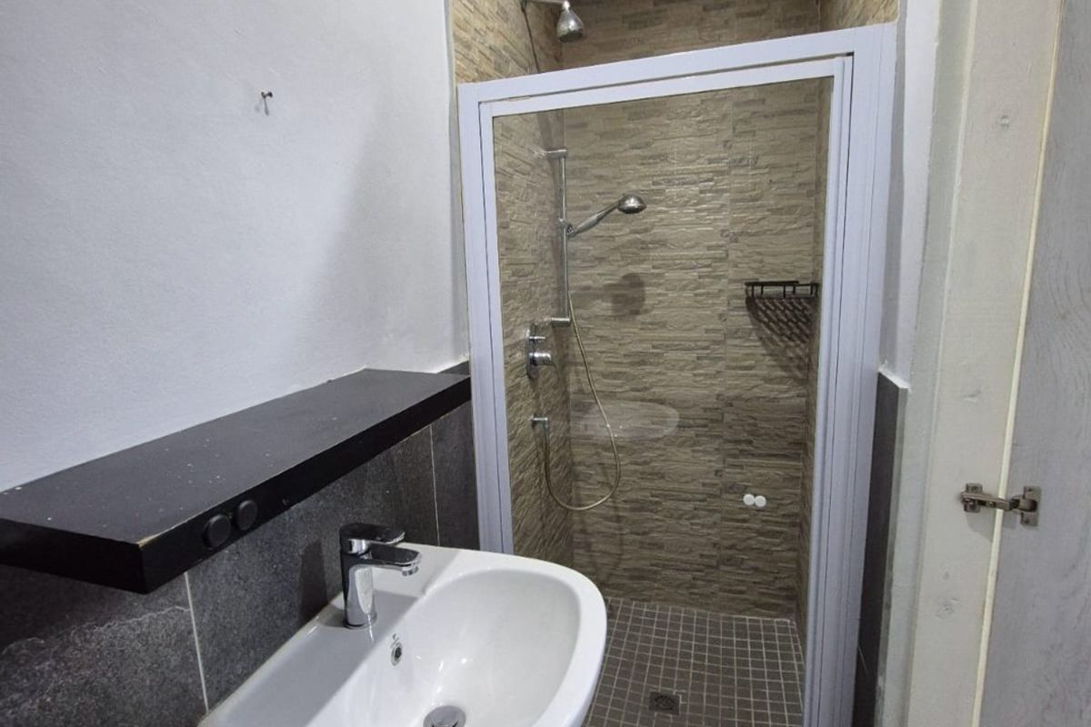 A compact bathroom featuring a wall-mounted basin, a tiled shower enclosure with a glass door, and modern floor tiling.