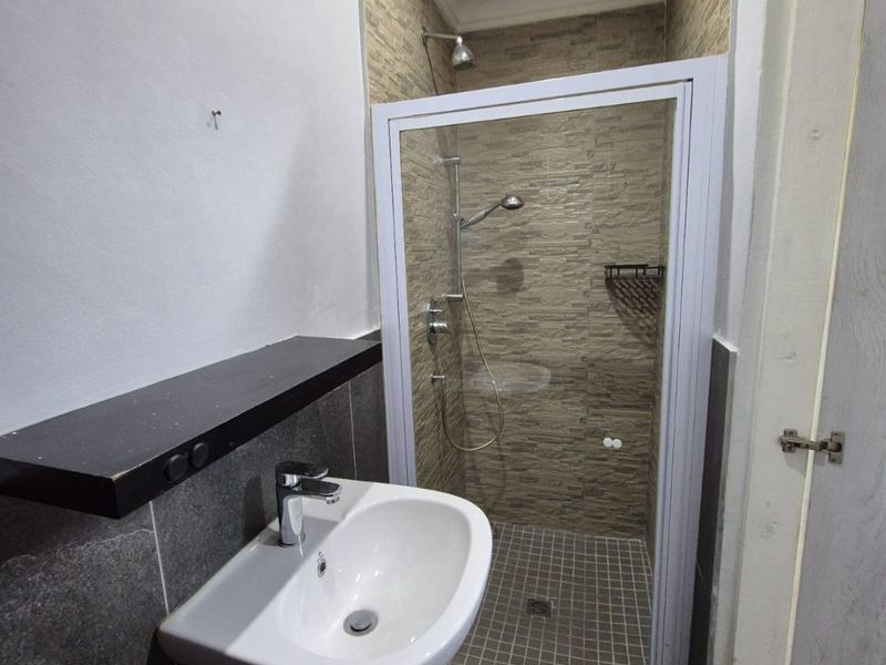 A compact bathroom featuring a wall-mounted basin, a tiled shower enclosure with a glass door, and modern floor tiling.