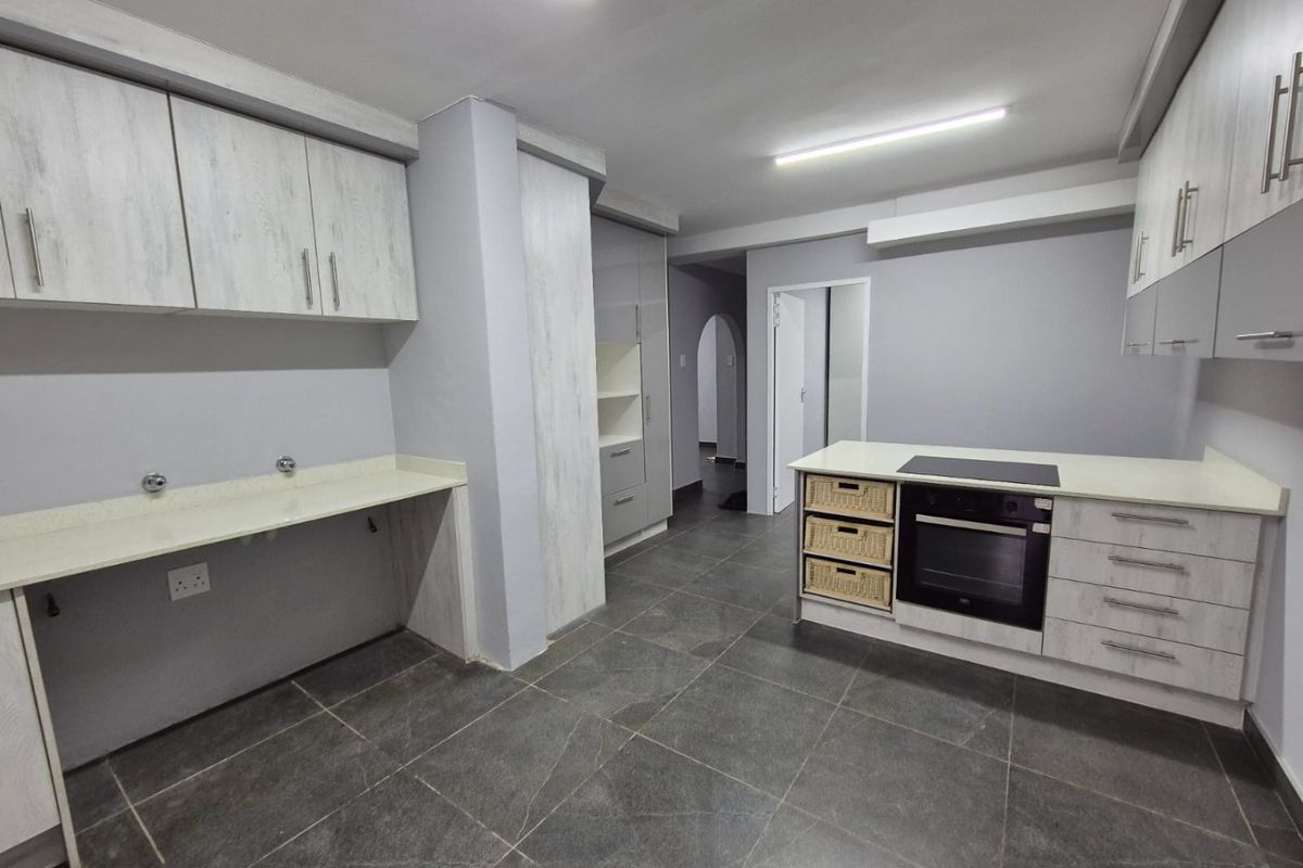 A modern, empty kitchen featuring light-toned cabinetry, stone countertops, a built-in oven, and dark tiled flooring.