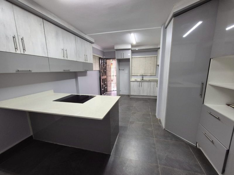 Modern kitchen featuring two-tone cabinetry, stone countertops with an integrated hob, tiled flooring, and a secondary prep area with a sink.