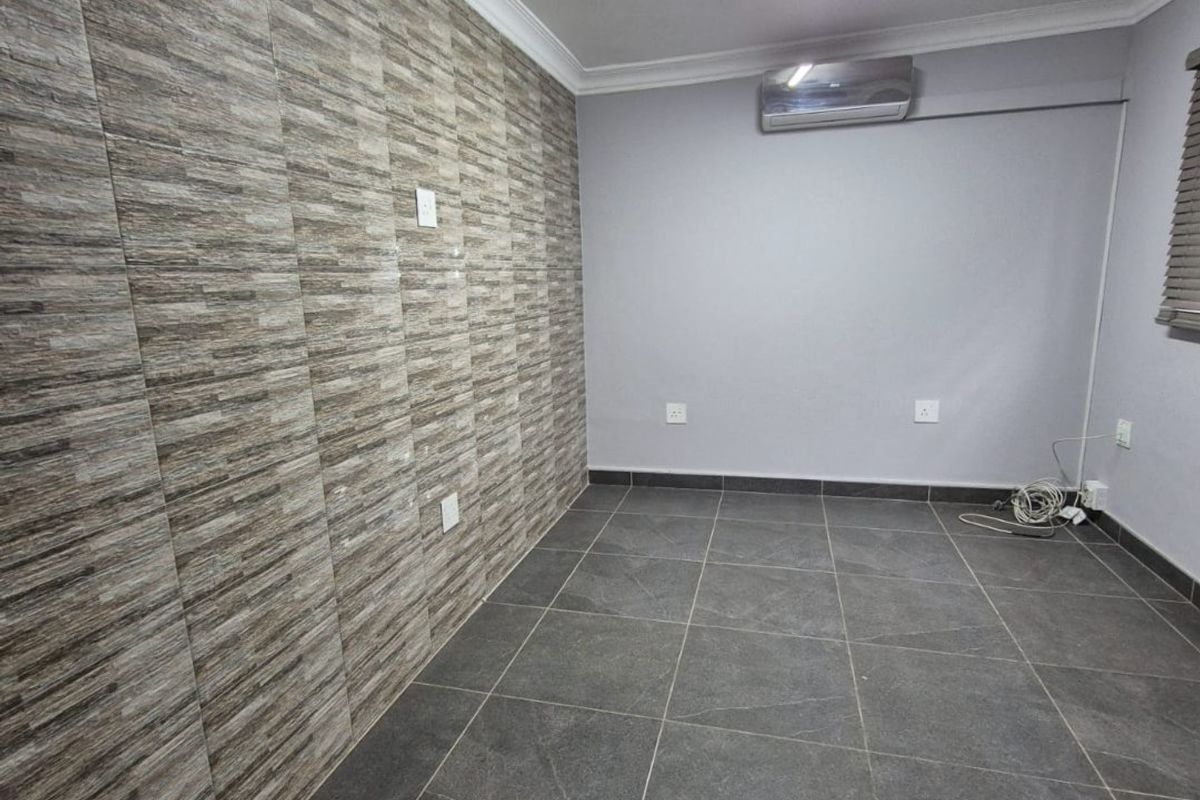 An empty living area featuring dark floor tiles, a textured feature wall, and a wall-mounted air conditioning unit.