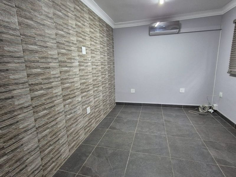 An empty living area featuring dark floor tiles, a textured feature wall, and a wall-mounted air conditioning unit.
