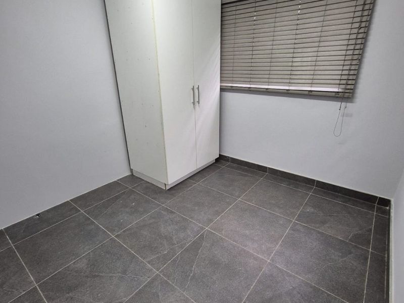 A clean, empty bedroom featuring modern dark grey floor tiles, neutral walls, built-in wardrobe storage, and venetian blinds.