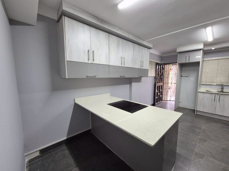 Modern kitchen featuring two-tone cabinetry, stone countertops, an integrated induction hob, and tiled flooring with direct access to an exterior security gate.
