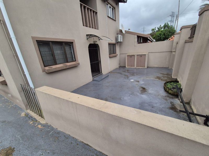 A paved rear courtyard area featuring a security gate, built-in storage, and an external air conditioning unit, enclosed by a boundary wall.