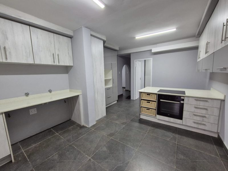 A modern, empty kitchen featuring light-toned cabinetry, stone countertops, a built-in oven, and dark tiled flooring.