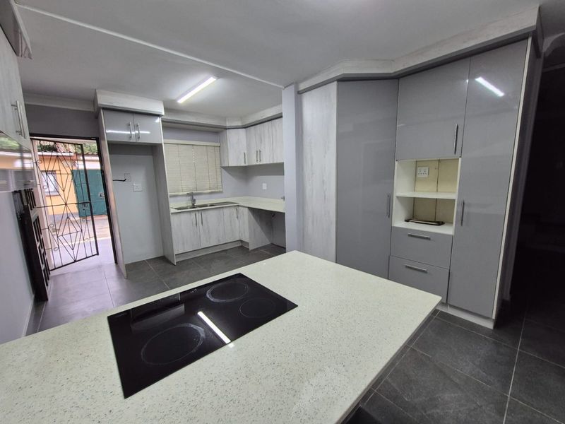 Modern kitchen featuring sleek grey cabinetry, stone countertops, a central island with an integrated electric hob, and tiled flooring.