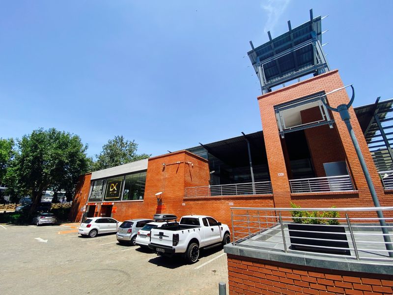 A commercial building featuring a prominent brick facade, a distinctive tower structure, and an adjacent paved parking area.