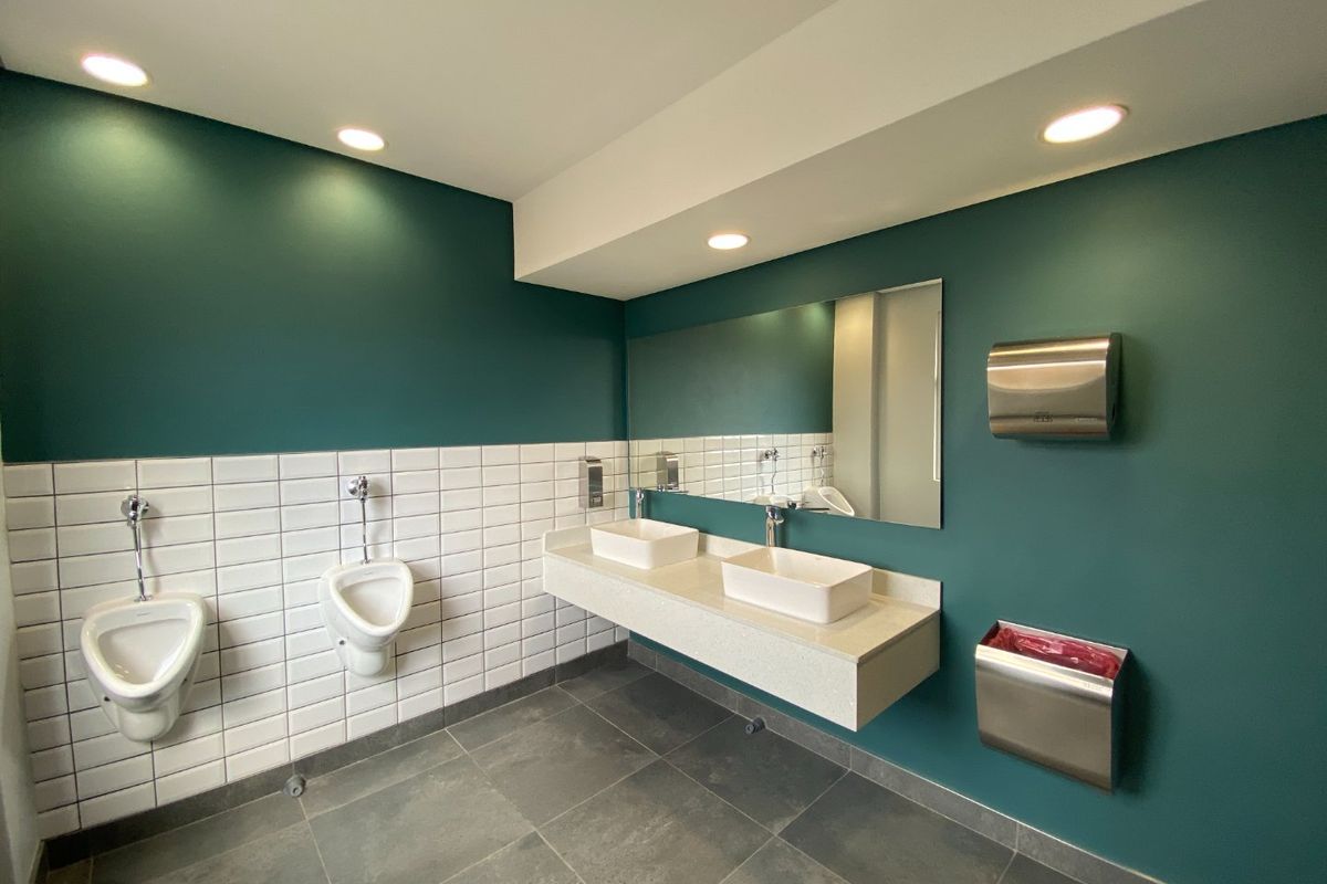 Modern commercial restroom featuring dual vessel sinks on a floating vanity, wall-mounted urinals, and contemporary teal and white tiled finishes.