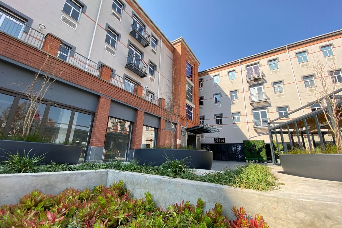 A view of the commercial building's rear courtyard area, featuring multi-story brick and render facade with balconies and integrated concrete landscaping.
