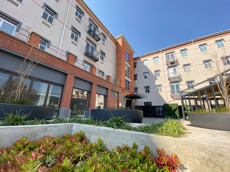 A view of the commercial building's rear courtyard area, featuring multi-story brick and render facade with balconies and integrated concrete landscaping.