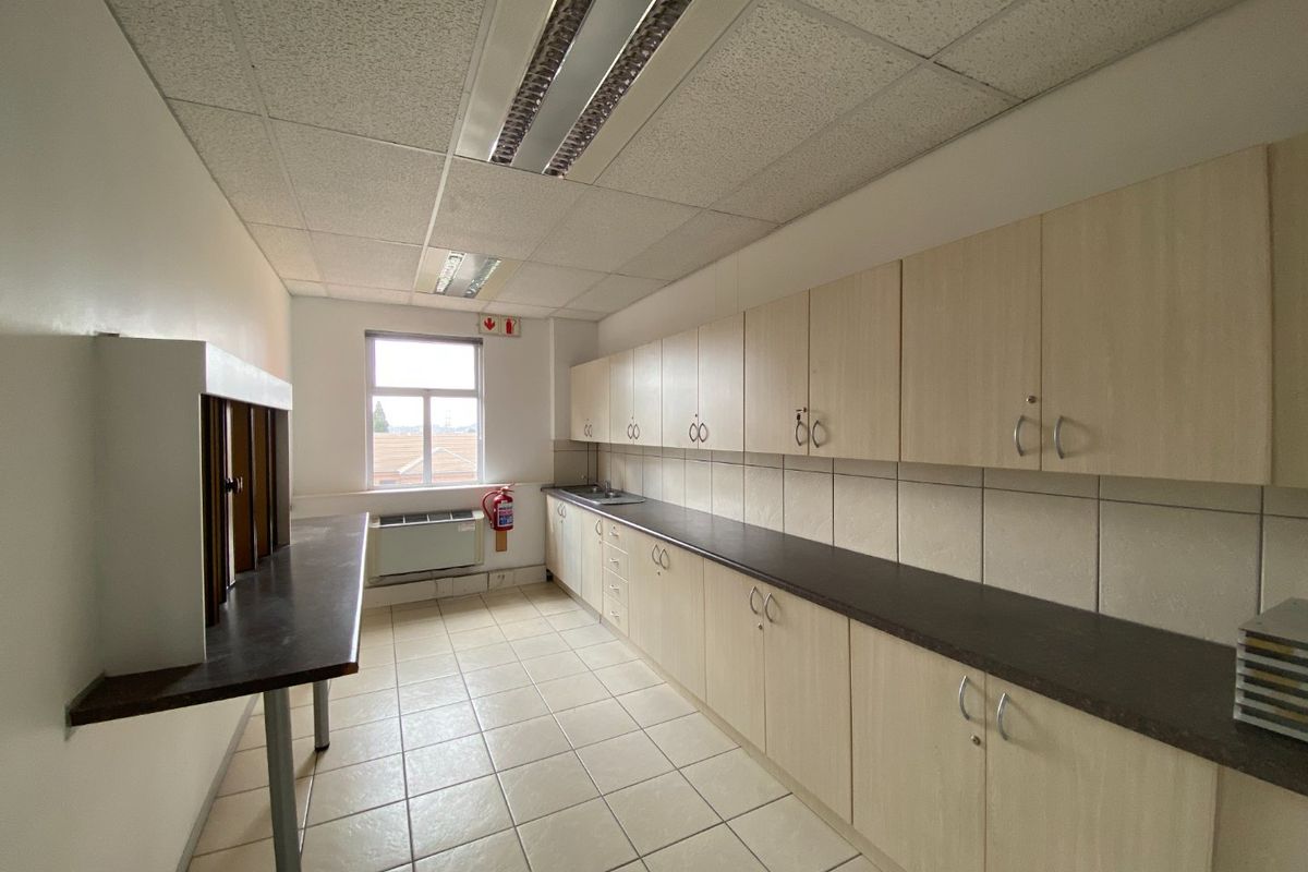 A functional commercial kitchenette featuring extensive laminate cabinetry, dark countertops, ceramic tile flooring, and integrated fluorescent lighting.