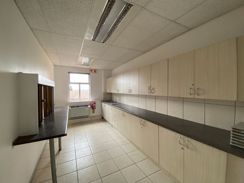 A functional commercial kitchenette featuring extensive laminate cabinetry, dark countertops, ceramic tile flooring, and integrated fluorescent lighting.