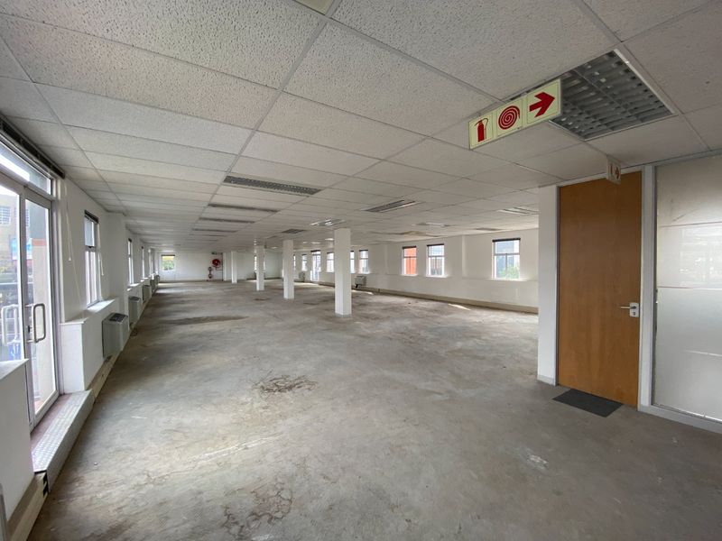 A large, open-plan commercial office space featuring a suspended ceiling, recessed lighting, and multiple windows, currently awaiting flooring finishes.