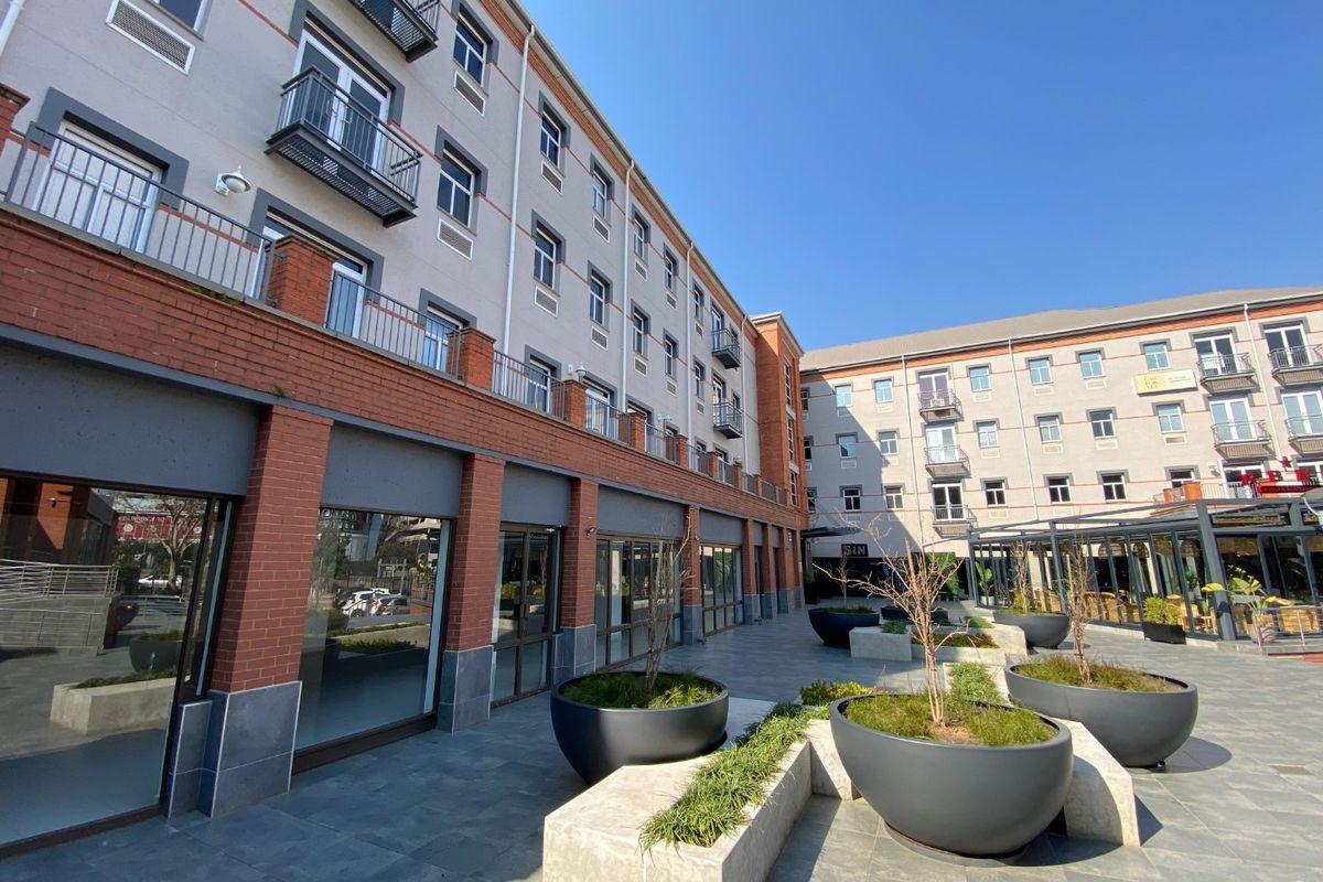 A well-maintained commercial courtyard featuring paved surfaces, built-in planters, and multi-story building facades with balconies and large glass storefronts.