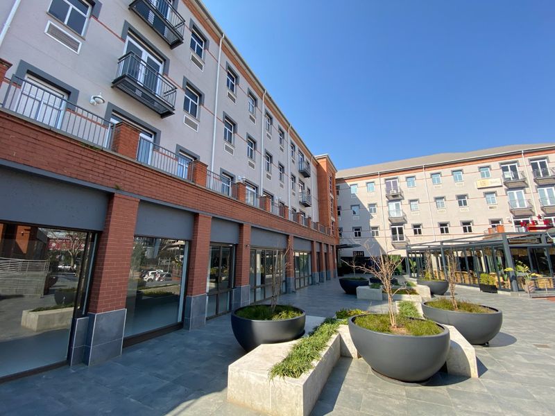 A well-maintained commercial courtyard featuring paved surfaces, built-in planters, and multi-story building facades with balconies and large glass storefronts.
