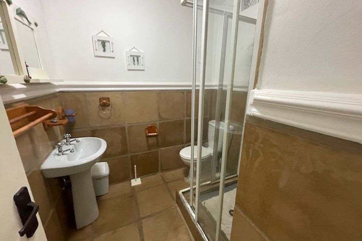 A functional bathroom featuring a pedestal basin, a glass-enclosed shower, and a toilet, finished with neutral floor and wall tiling.