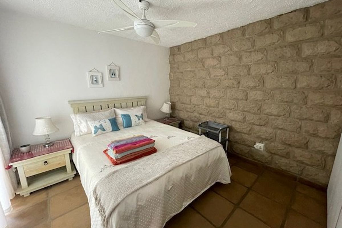 A bedroom featuring a rustic stone accent wall, terracotta floor tiles, and a ceiling fan.