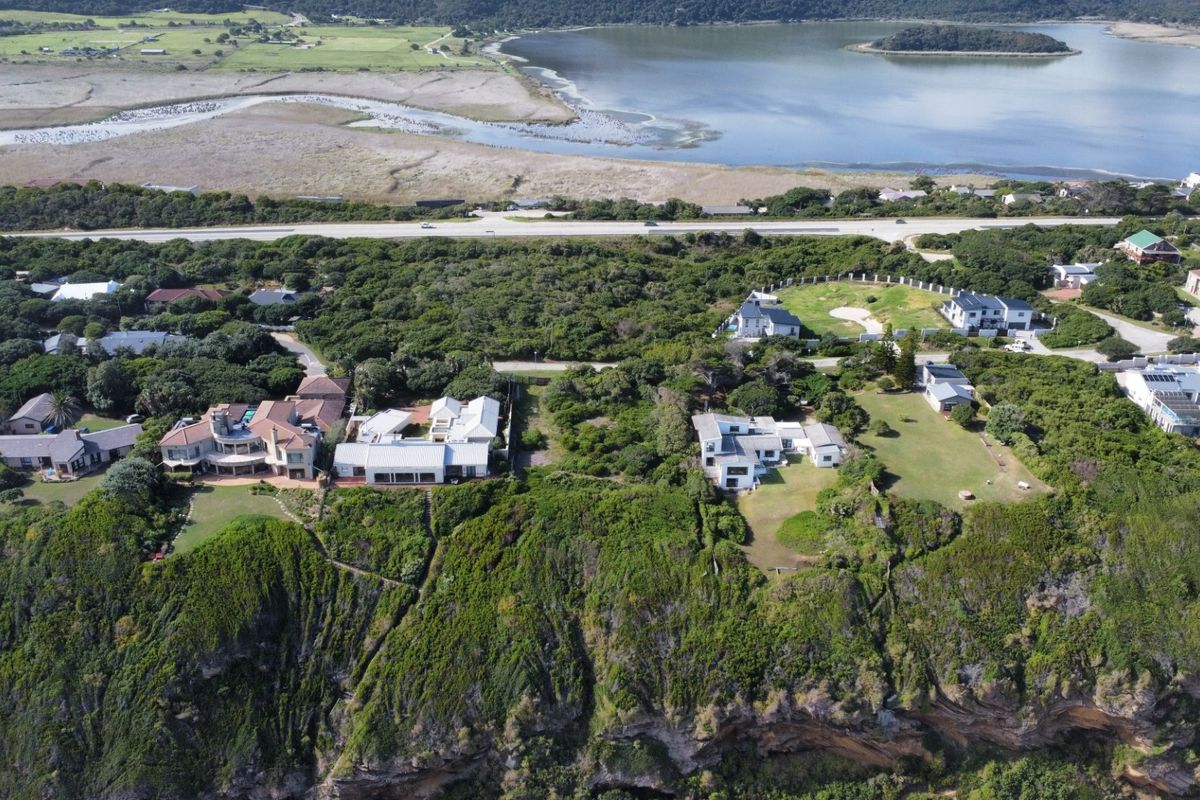 An aerial view of a coastal residential area featuring cliffside properties, lush vegetation, and proximity to a lagoon and main road.
