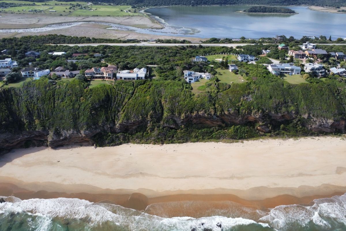 An aerial view of the coastal residential area, showcasing the cliffside location, sandy beach, and proximity to the ocean.