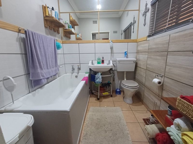 A functional bathroom featuring a bathtub, pedestal basin, toilet, and tiled finishes, offering a practical layout with potential for modern cosmetic updates.