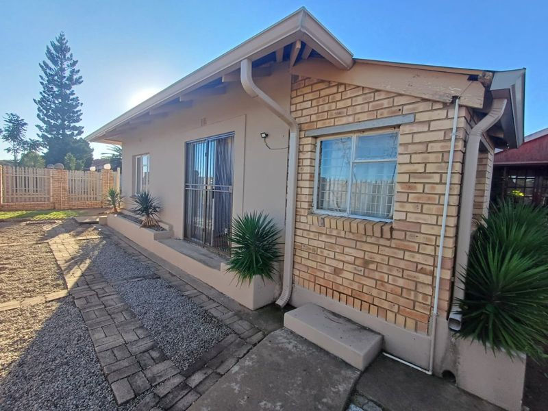 Rear exterior view of the house featuring brick and plastered walls, sliding door access, security bars, and a paved walkway with gravel garden area.