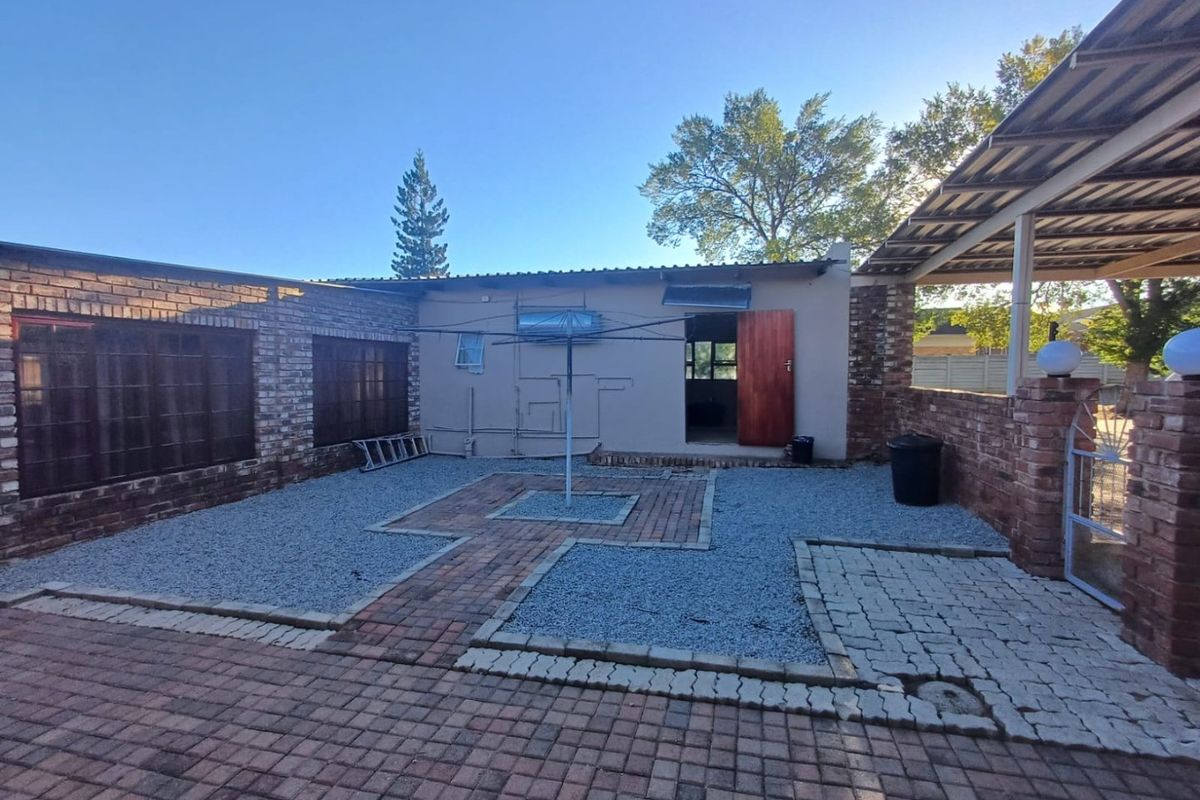 A rear courtyard area featuring a combination of brick paving and gravel, with a covered patio section and an exposed brick boundary wall.