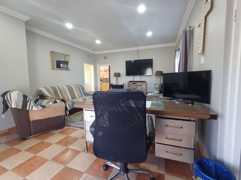 A living room featuring tiled flooring, recessed downlighting, and a tongue and groove ceiling, offering a functional space for relaxation or home office use.