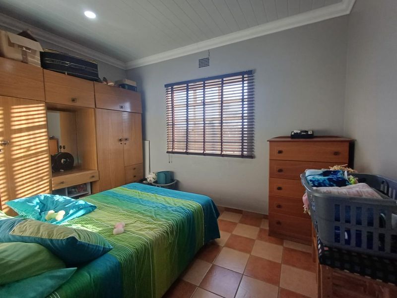A bedroom featuring built-in wooden cupboards, tiled flooring, and venetian blinds, offering a functional space with neutral wall tones.