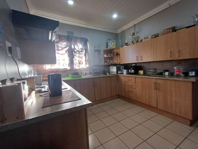 A functional kitchen featuring laminate cabinetry, ample countertop space, a stainless steel sink, and tiled flooring, offering a practical layout for daily meal preparation.
