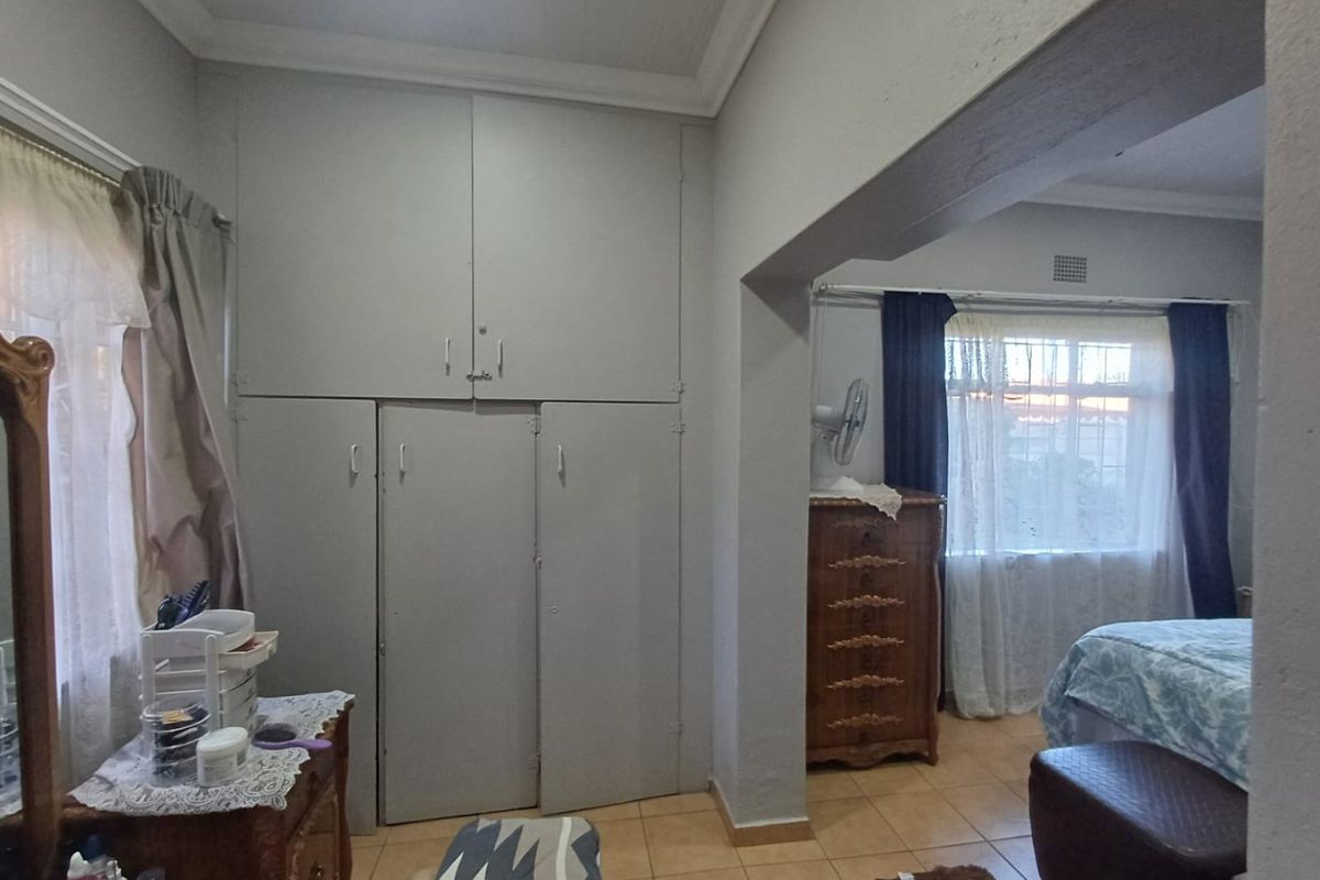 A bedroom featuring built-in cupboards, tiled flooring, and large windows with security bars, offering a functional layout with potential for modernization.