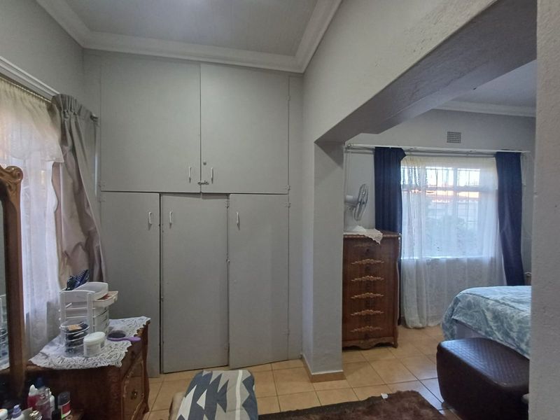 A bedroom featuring built-in cupboards, tiled flooring, and large windows with security bars, offering a functional layout with potential for modernization.