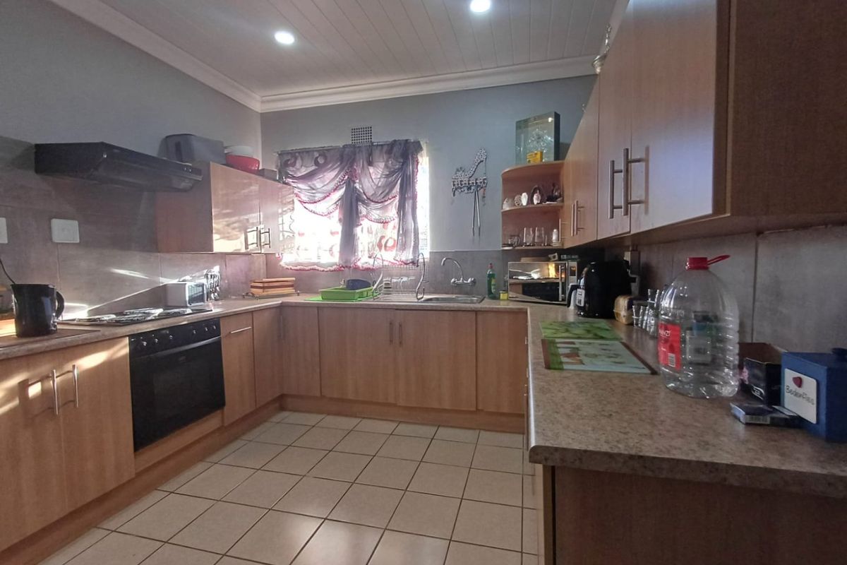 A functional kitchen featuring light wood-finish cabinetry, laminate countertops, built-in oven with hob, and tiled flooring under a tongue and groove ceiling.