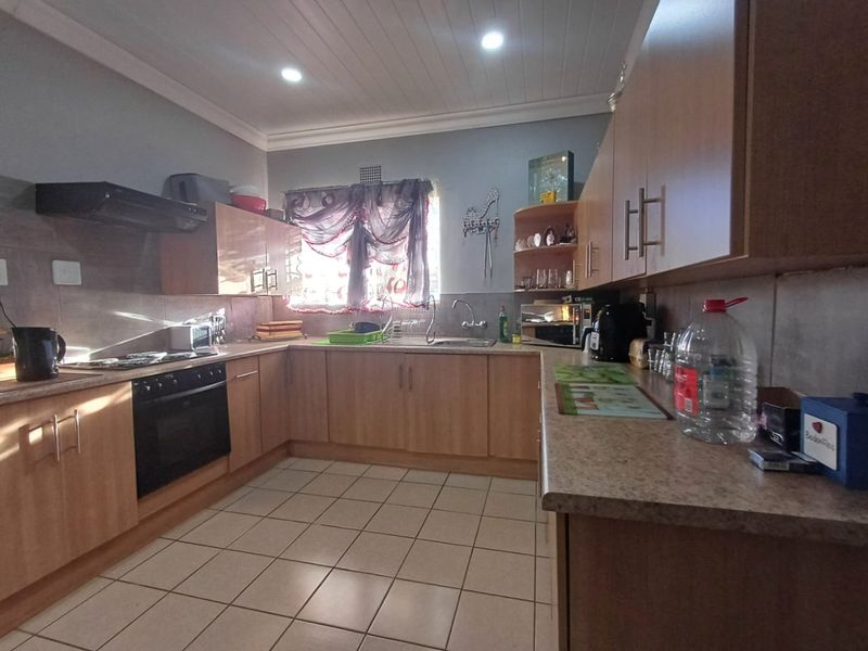 A functional kitchen featuring light wood-finish cabinetry, laminate countertops, built-in oven with hob, and tiled flooring under a tongue and groove ceiling.