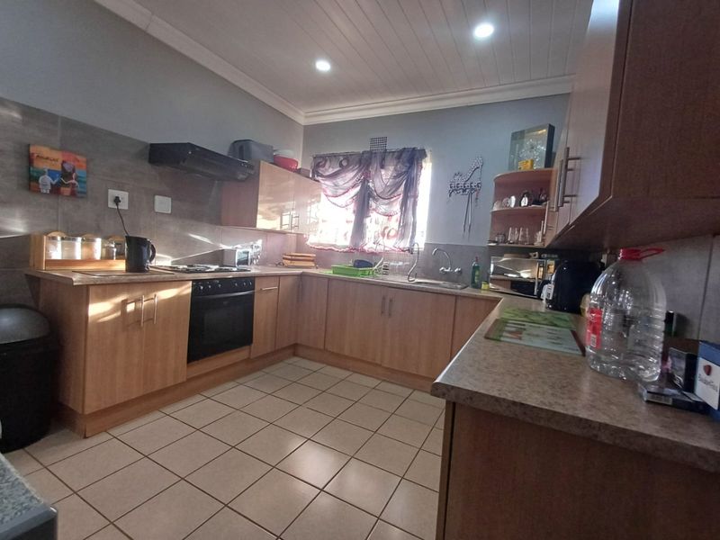 Functional kitchen featuring wood-look cabinetry, laminate countertops, built-in oven with gas hob, extractor fan, and tiled flooring.