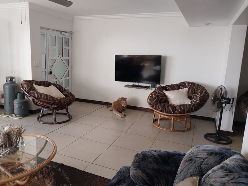 A living room featuring neutral tiled flooring, a wall-mounted television, and a decorative glass panel door, offering a functional and open living space.