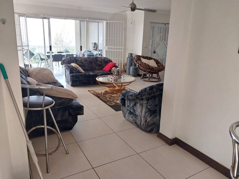 Spacious living area featuring neutral tiled flooring, a ceiling fan, and large sliding glass doors that provide access to an outdoor patio space.