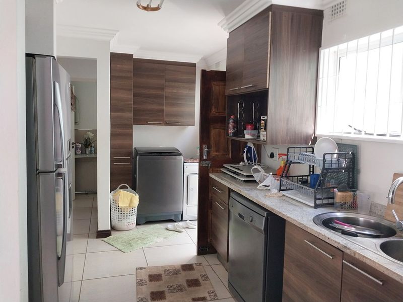 Functional kitchen featuring wood-look cabinetry, stone-effect countertops, double sink, and tiled flooring with an adjacent laundry area.
