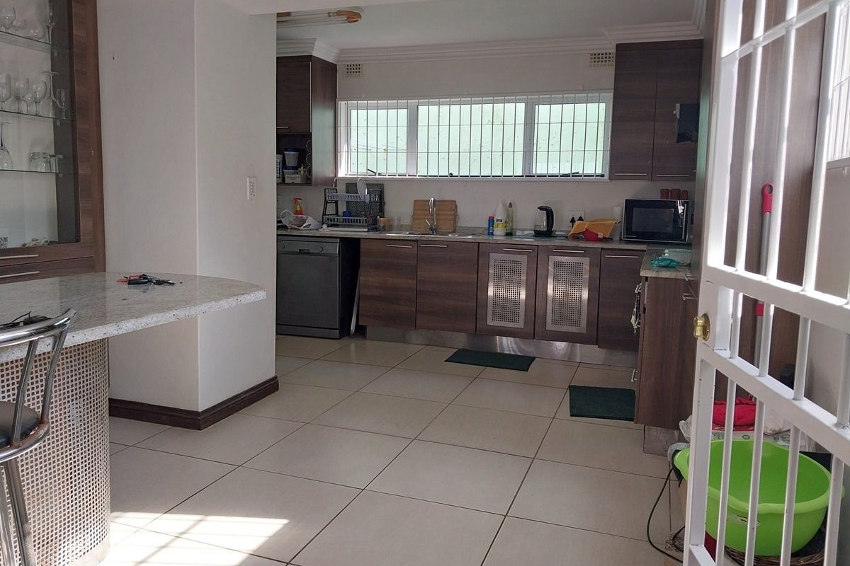 A functional kitchen featuring wood-finish cabinetry, granite countertops, a breakfast bar, and tiled flooring, with security bars installed on the windows.