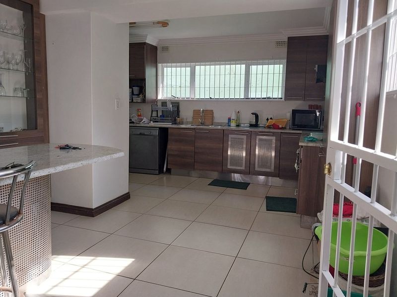 A functional kitchen featuring wood-finish cabinetry, granite countertops, a breakfast bar, and tiled flooring, with security bars installed on the windows.