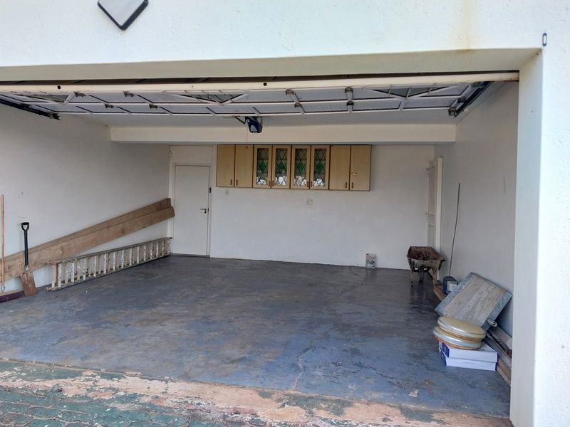 A spacious double garage featuring built-in wall cabinetry, concrete flooring, and direct internal access, offering ample storage and parking potential.