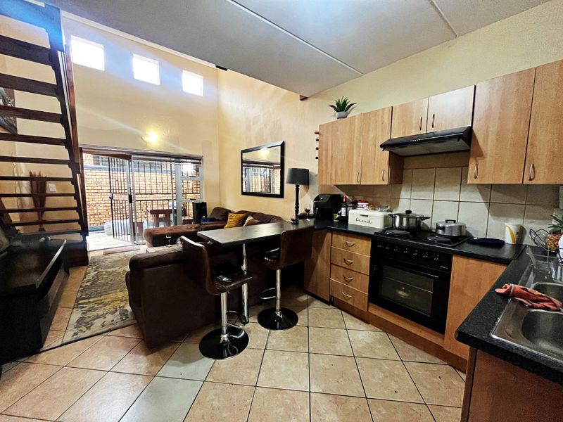 Open-plan living area featuring a kitchen with built-in cabinetry, oven, and hob, flowing into a lounge space with staircase access and sliding door to patio.