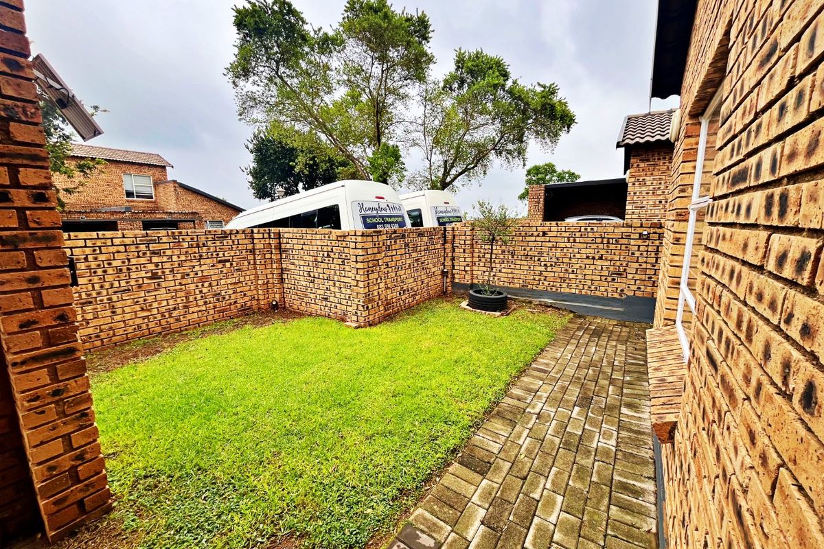 A private rear garden area featuring a well-maintained lawn, paved walkway, and secure face brick boundary walls.