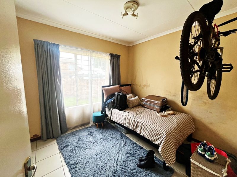 A bedroom featuring tiled flooring and security bars on the window, currently showing signs of wall wear and paint deterioration.
