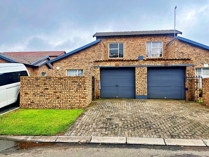 Front elevation of a double-story townhouse featuring a double garage, paved driveway, and face-brick exterior finish.
