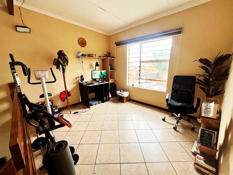 A functional office space featuring tiled flooring and a large window with security bars, providing natural light and a view of the exterior.