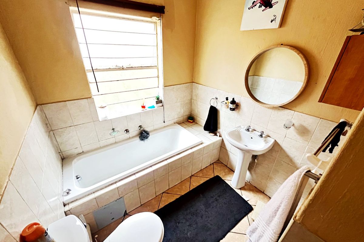 A functional bathroom featuring a bathtub, pedestal basin, toilet, and tiled finishes, offering a practical layout with natural light from a louvered window.